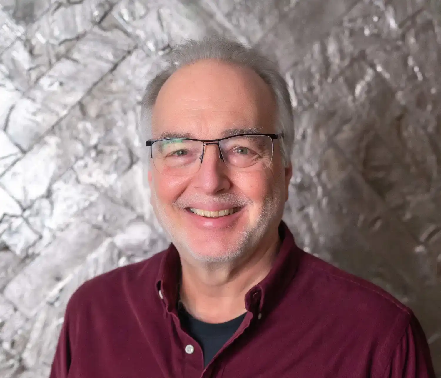 Man in glasses smiling against a metallic textured background.