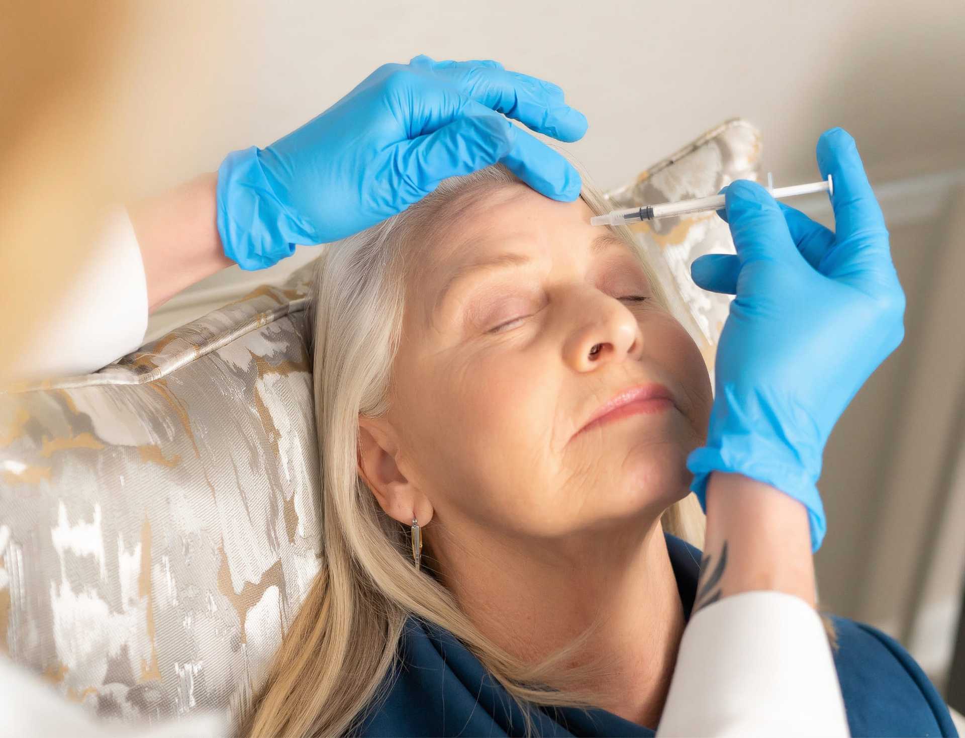 Elderly woman receiving a facial injection from a medic in gloves.