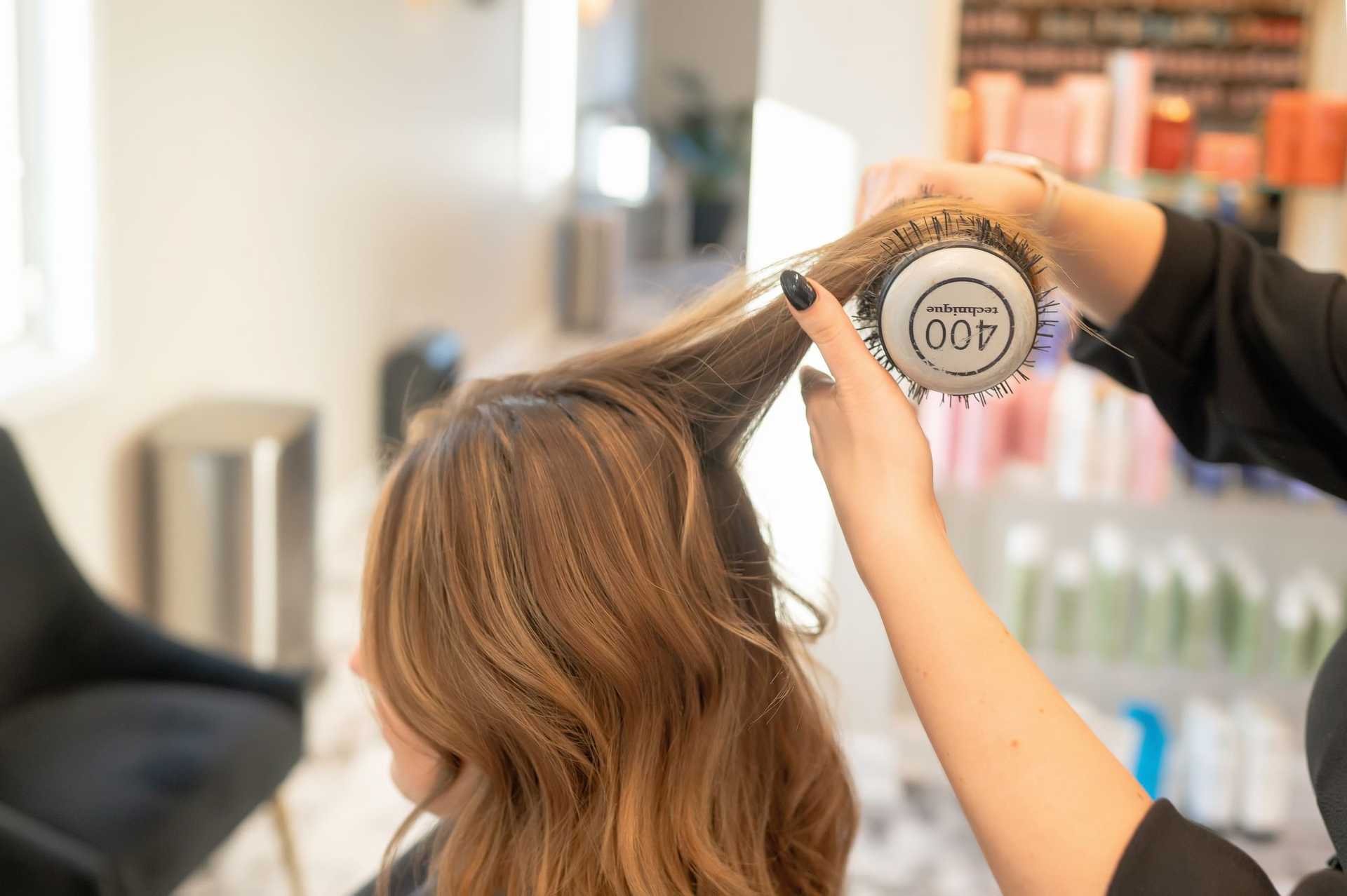 Hairdresser styling a client's hair with a round brush.